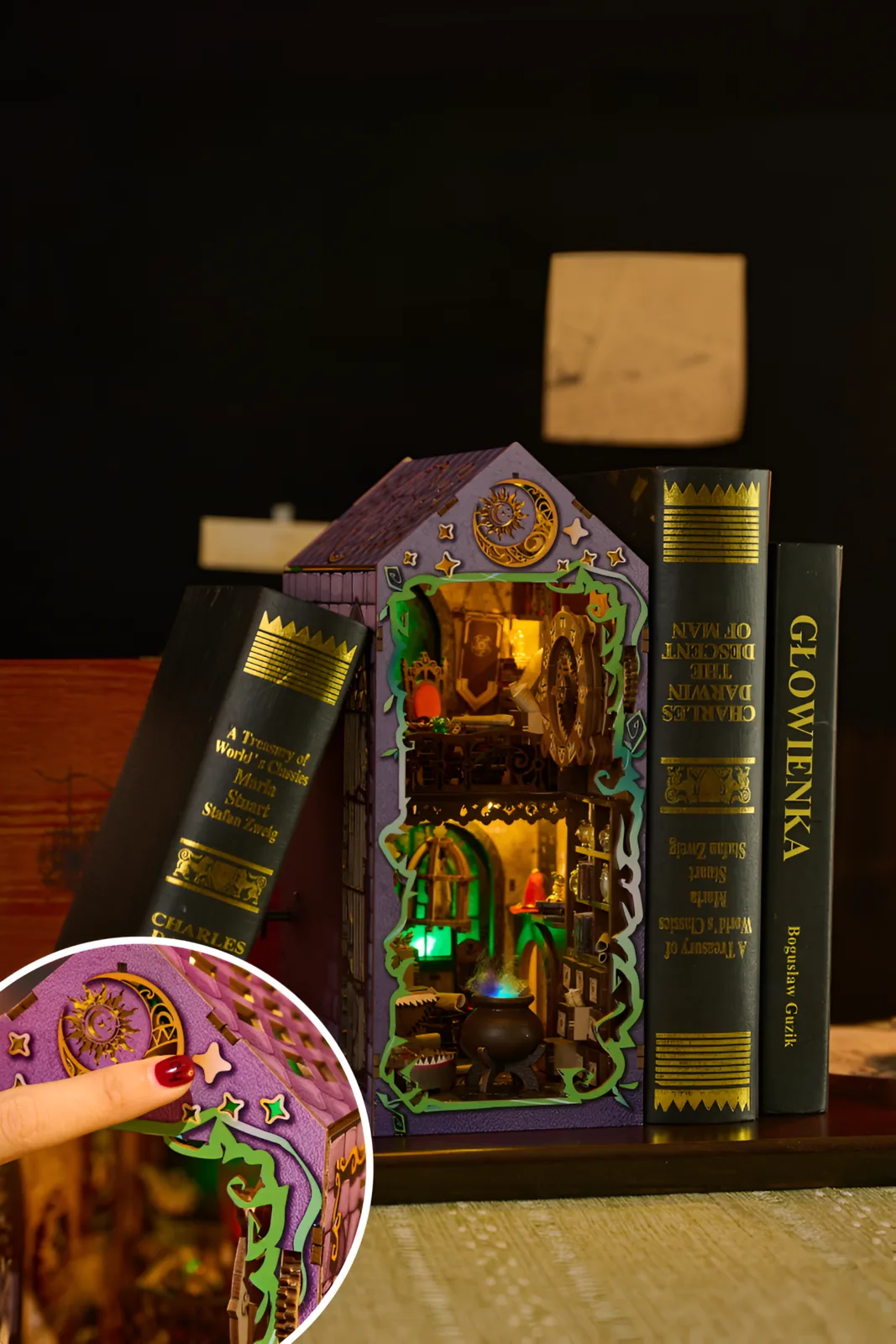 The Witches House miniature glowing green and gold between books on a shelf, with a bubbling cauldron inside.